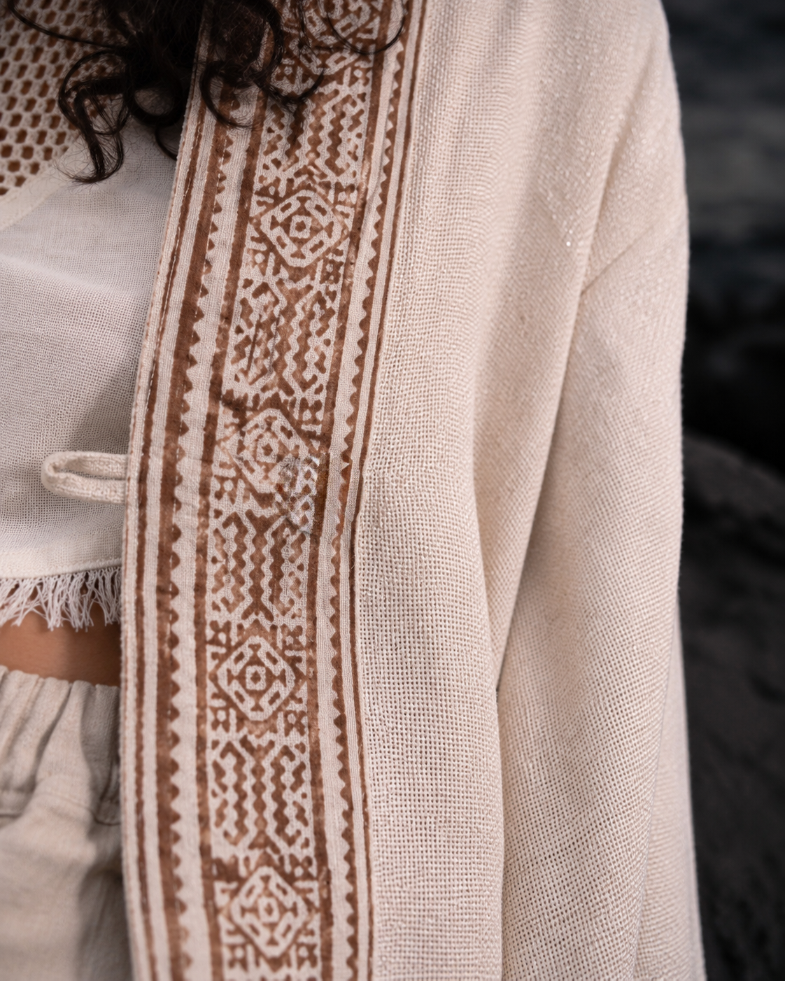 Close-up of a cream-colored textured jacket with a wide brown geometric embroidered border, worn by a model.