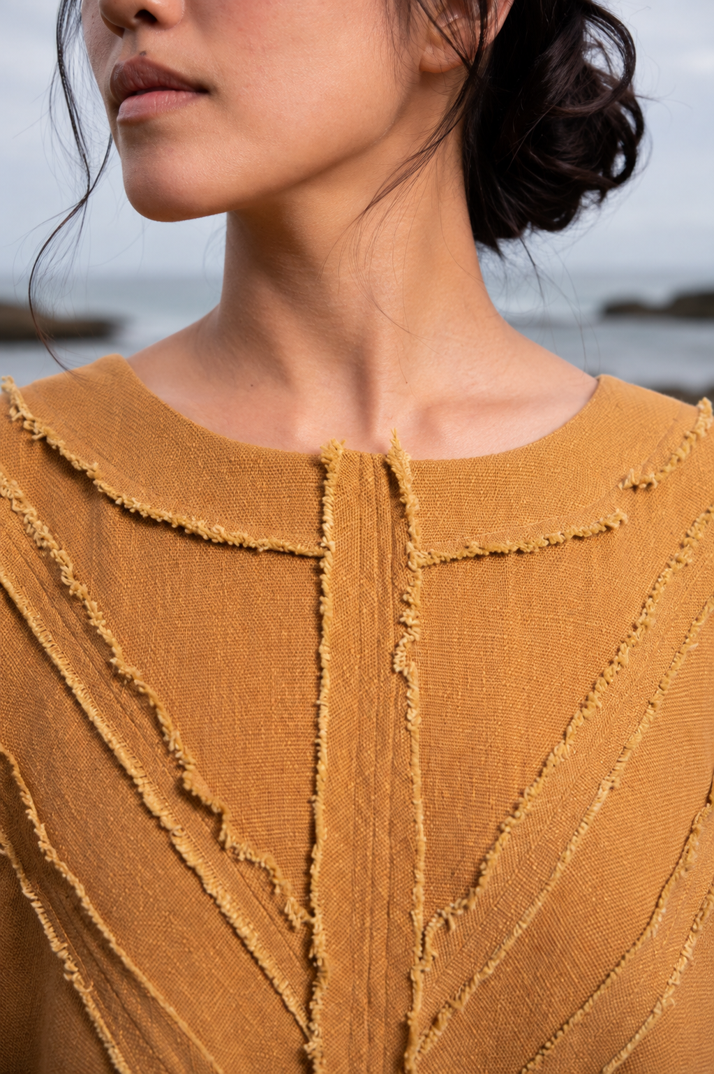 Close-up of a model wearing a textured mustard yellow knit top with a raw, frayed collar and vertical textured paneling.