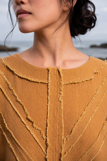 Close-up of a model wearing a textured mustard yellow knit top with a raw, frayed collar and vertical textured paneling.