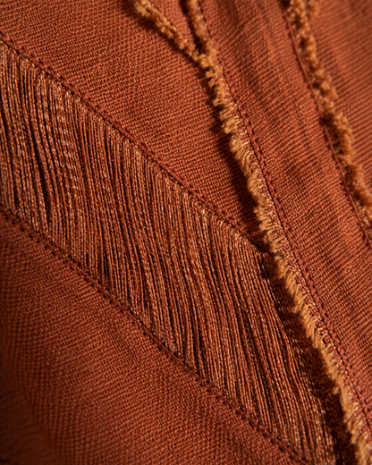 Close-up of a rust-brown woven textile with diagonal fringe and raw, frayed edges.
