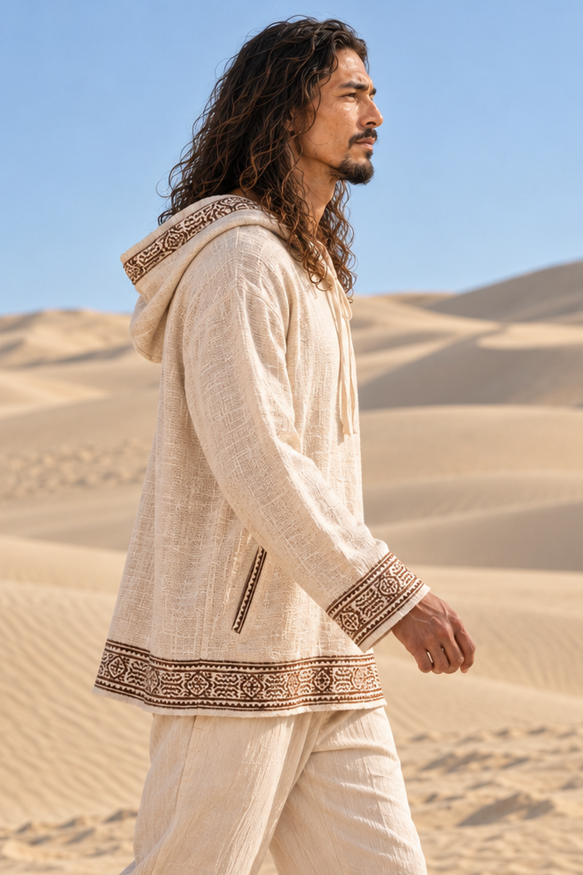 Side profile of man walking in beige block-printed cotton hoodie, hood down, showing the pocket and cuff trim