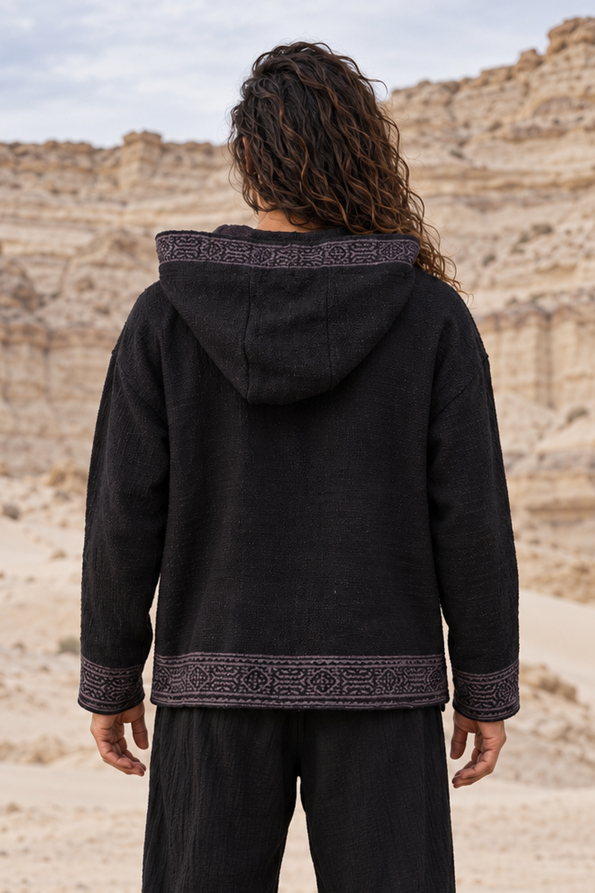 Back view of black cotton hoodie with hood down, grey hand-stamped trim along the hood edge, cuffs and hem