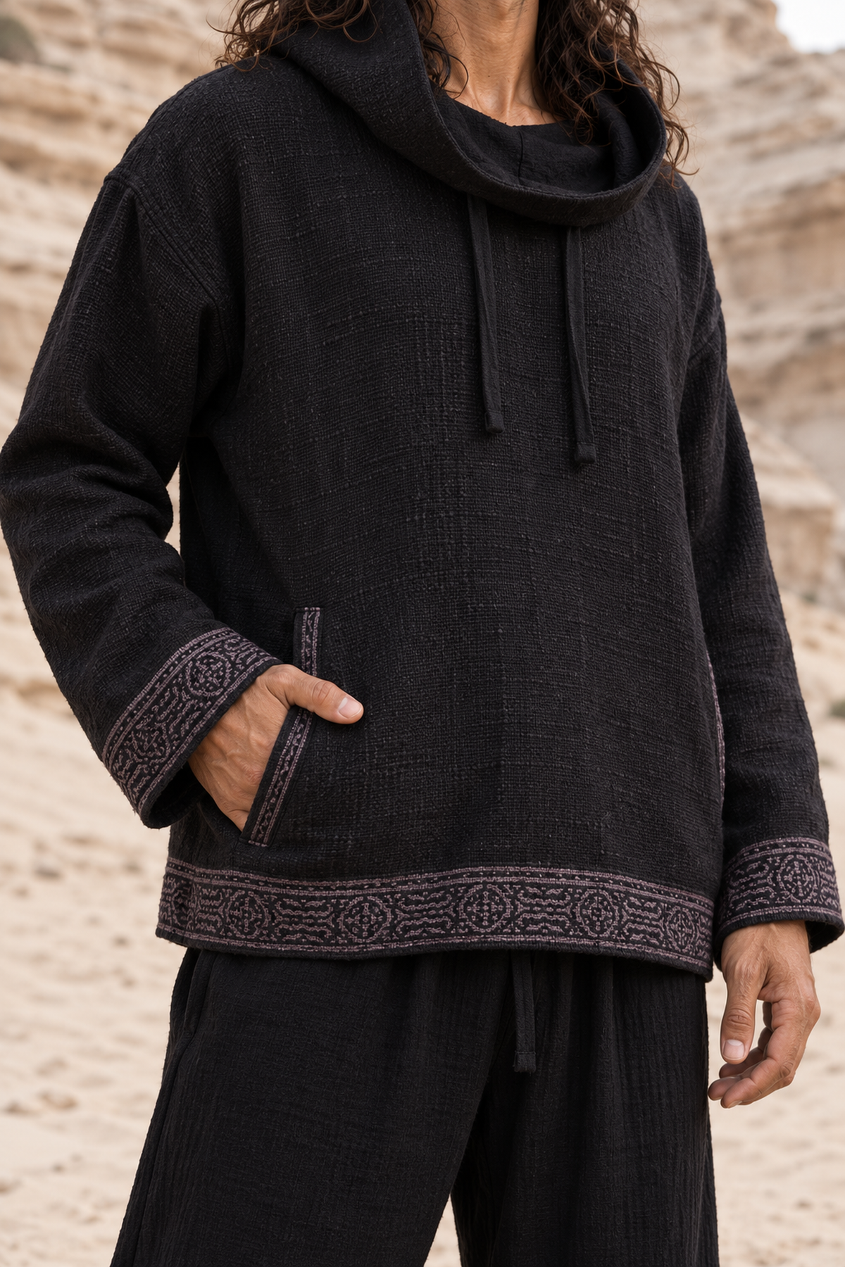 Black handwoven cotton hoodie worn with the hood down as a cowl, hand in front pocket, grey block-printed cuffs and hem