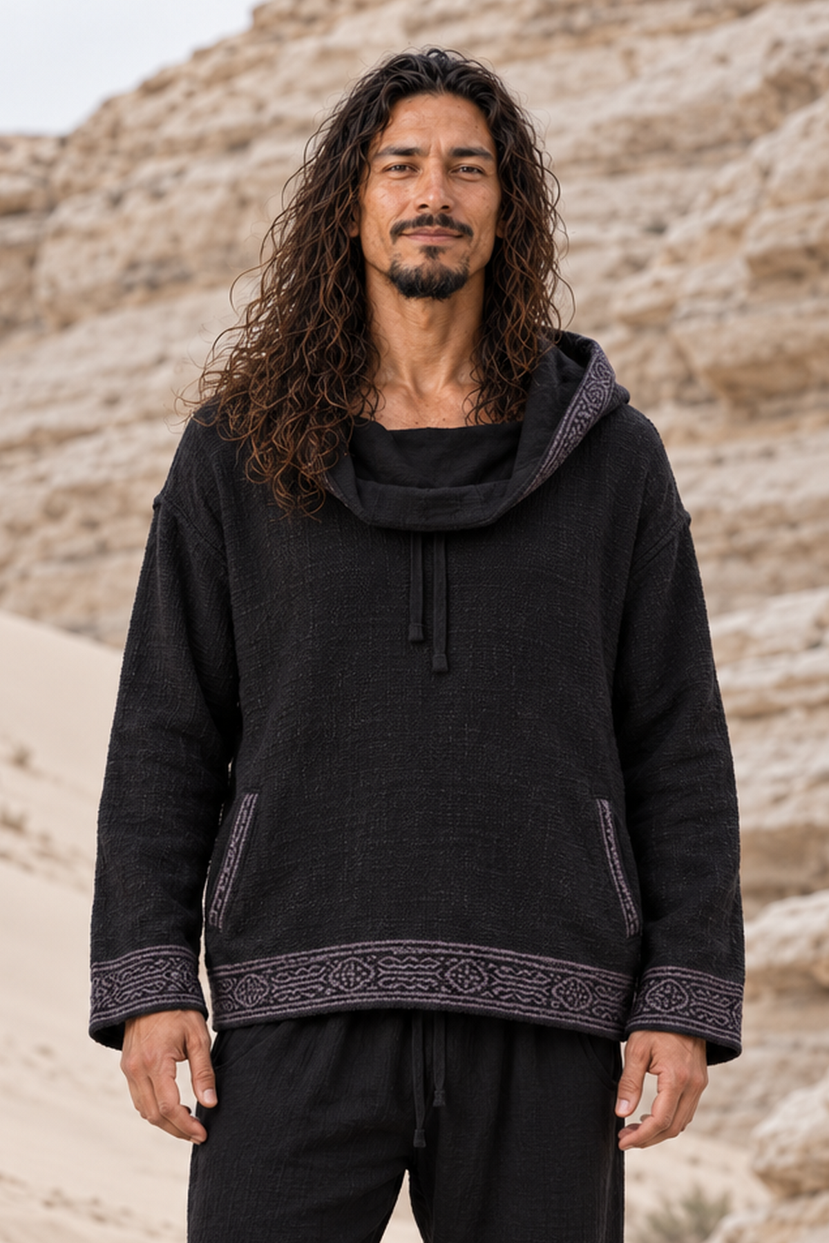 Front view of man in black block-printed cotton hoodie, hood down as a loose cowl neck, drawstring and pockets visible