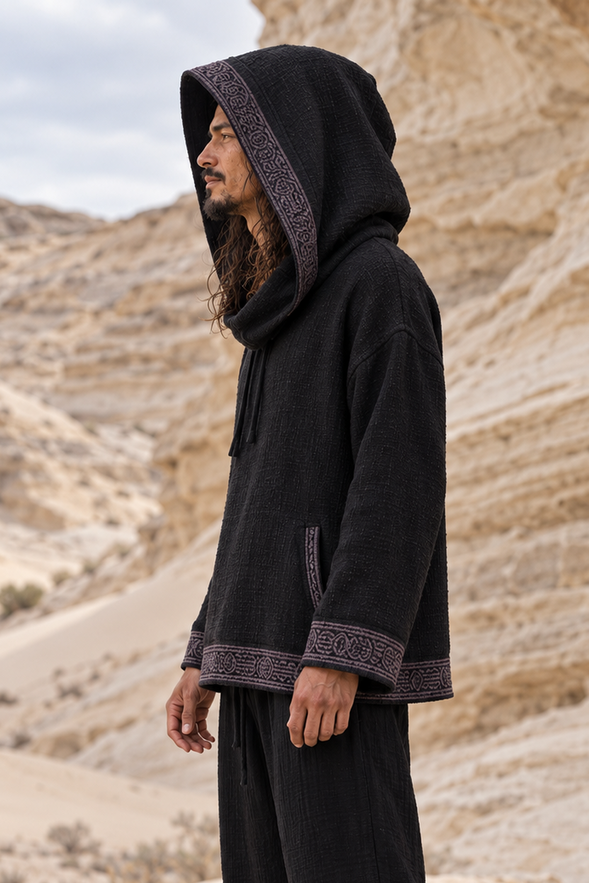 Side profile of man in black cotton hoodie with the hood up, grey block-printed band edging the hood, cuffs and hem
