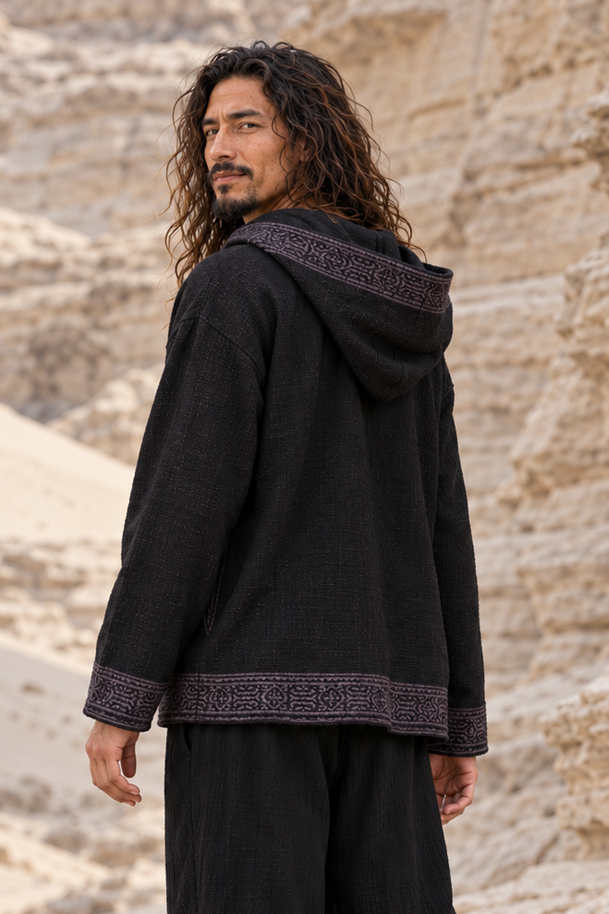 Man looking back over his shoulder in black block-printed cotton hoodie, hood down, showing the back and hem trim