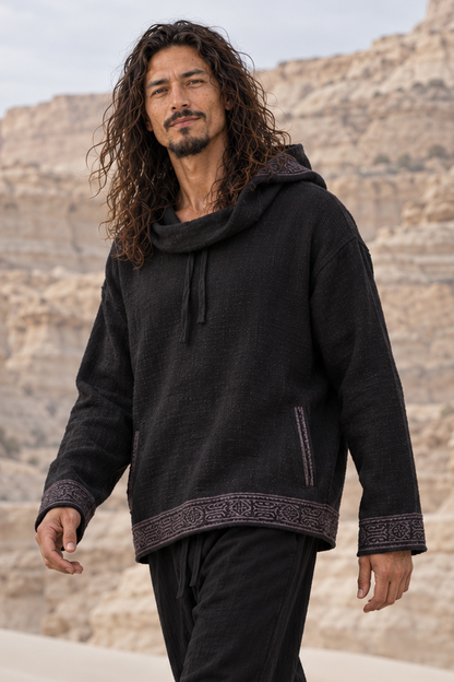 Man walking in black SUKKUN cotton hoodie, hood down, grey block-printed bands at the cuffs and hem